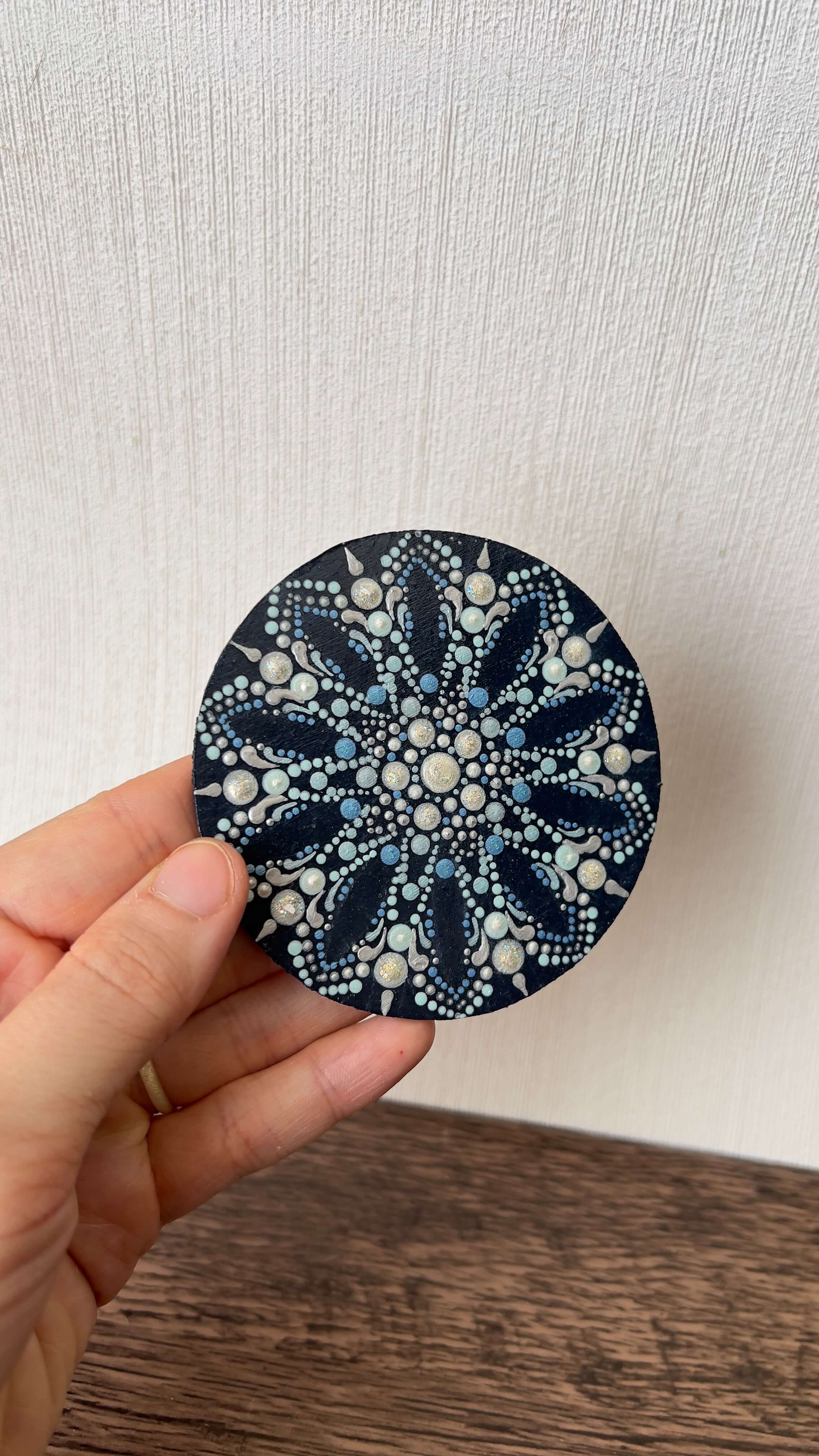Snowflake dot mandala coaster with various shades of blue and white sparkly paint